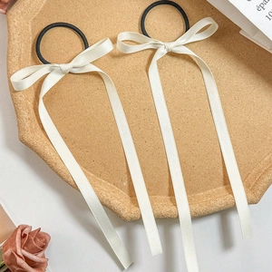 Detail view of two cream white ballet style ribbon bow hair ties in a felt tray