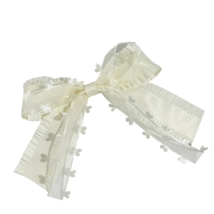 Detail of sheer ivory ribbon hair clip with delicate wavy edges and heart appliques