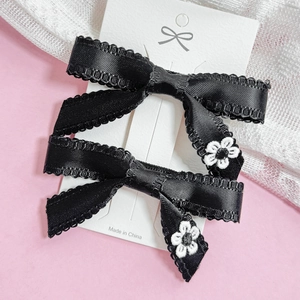 Detail of two black silk bow hair clips with white flower embroidery on pink backdrop
