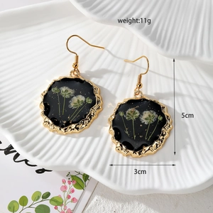Detail view of round black resin earring with white dried flowers and gold metal trim