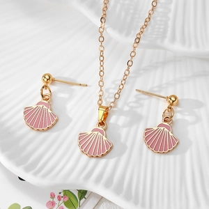 Detailed shot of gold shell jewelry set with pink enamel on a textured ceramic plate
