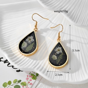 Detail view of teardrop earrings with white dried flowers and gold leaf in black resin