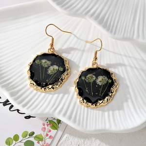 Golden hook earrings with dark resin pendants featuring real dried daisy flower details