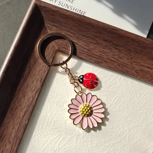 Porte-clés marguerite et coccinelle avec chaîne dorée sur fond de bois