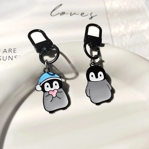 Detail of two cute alloy penguin keychains with blue hat and pink heart in a white tray