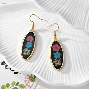 Detailed close-up of handmade oval resin earrings featuring real dried flowers and gold foil