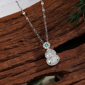 Detail of hulu gourd pendant with white stone inlay and green gem on dark wood