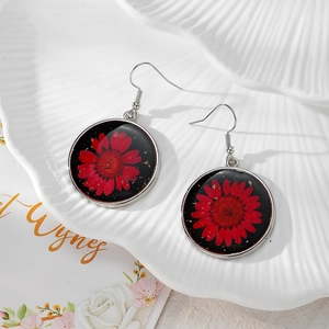 Detailed close-up of handmade resin daisy earrings with gold foil and red dried flowers