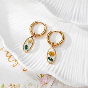 Detailaufnahme vergoldeter Ohrringe mit echten gelben Trockenblumen in Harzanhängern