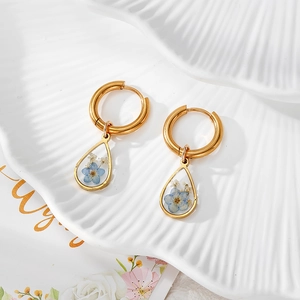 Detailaufnahme der goldenen Tropfenohrringe mit echten blau-weißen Trockenblumen