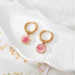 Nahaufnahme goldener Harzohrringe mit echten rosa Trockenblumen auf weißem Teller