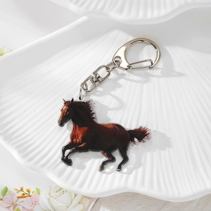 Detailed macro view of an acrylic horse keychain with silver metal clasp on a ceramic tray