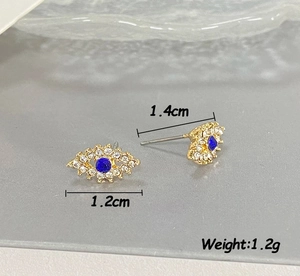 Vue macro de boucles d'oreilles Evil Eye dorées avec strass blancs et cristaux bleus