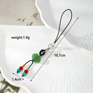 Detail shot of a green ruyi pendant phone strap with size info on ceramic background