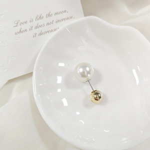 Spilla minimalista con perla e sfera dorata su un piatto decorativo a forma di conchiglia