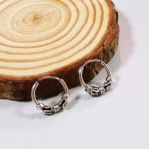 Vintage silver hoop earrings with intricate floral carvings on natural wood background