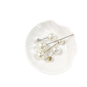 Elegante spilla con perle bianche e steli in metallo argento e oro in un piatto a conchiglia