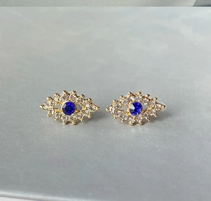 Détail des boucles d'oreilles œil porte-bonheur dorées avec cristal bleu et strass blancs
