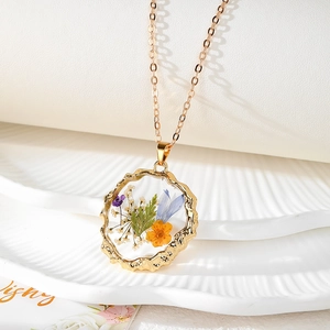 Détail d'un pendentif en résine aux fleurs séchées avec un bord doré martelé sur plateau