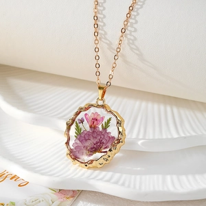 Vue détaillée d'un collier pendentif en fleurs séchées dorées sur une assiette blanche
