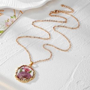 Détail du pendentif rond en résine dorée avec fleurs séchées mauves et chaîne or
