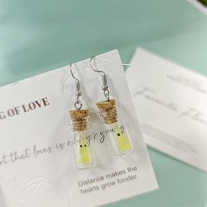 Détail de boucles d'oreilles bouteilles en verre avec pendentif fantôme jaune lumineux