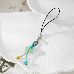 Detailed view of Chinese style jade gourd phone charm with woven cord on shell plate