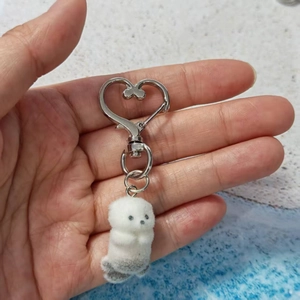 Close-up of white plush sea otter keychain with silver heart-shaped metal clasp
