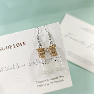 Gros plan de boucles d'oreilles bouteille miniature avec bouchon sur carte blanche