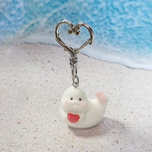 Detail of cute white flocked seal keychain with red heart on a beach sand background