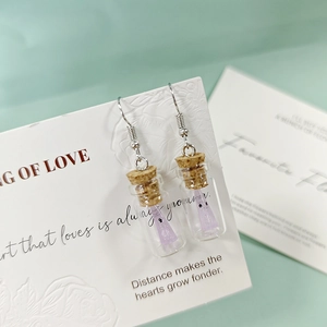 Détail de boucles d'oreilles mini bouteilles en verre avec bouchon et fantôme violet