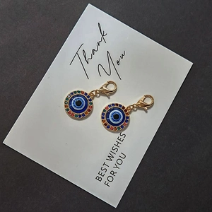 Detail of two evil eye charms with colorful rhinestones and lobster clasps on a white card