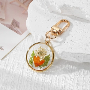 Macro detail of natural dried daisy and green leaves inside a round gold resin keychain