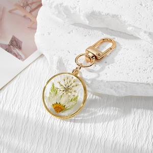 Golden round resin keychain featuring real white daisy and dried flowers in clear pendant