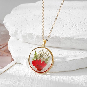 Vue macro du pendentif rond doré avec fleurs séchées rouges et blanches et feuilles vertes