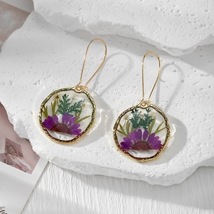 Pendientes de oro hechos a mano con flores secas púrpuras en resina sobre piedras
