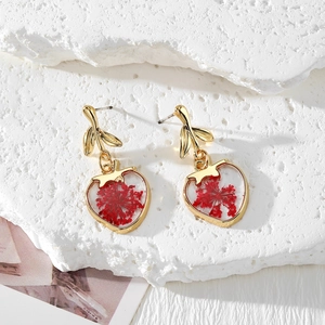 Detail of leaf-shaped studs and heart resin pendants with red dried flowers on white stone
