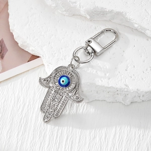 Silberner Hamsa-Hand-Schlüsselanhänger mit blauem Auge-Amulett auf weißem Stein