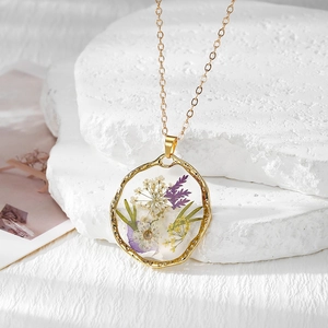 Détail d'un pendentif en résine dorée avec des fleurs séchées colorées et des feuilles