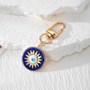 Golden sun and moon evil eye keychain with blue enamel inlay on textured stone background
