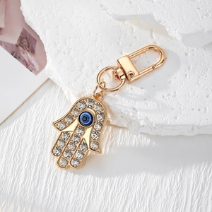 Porte-clés Main de Fatima dorée avec œil maléfique et strass sur un support en pierre