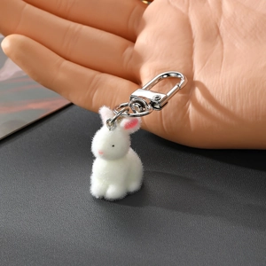 Détail d'un porte-clés lapin blanc floqué tenu en main montrant sa texture douce et sa taille