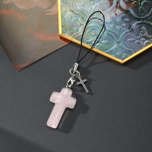 Détail du charm croix en résine rose pailletée avec pendentif argenté sur fond sombre