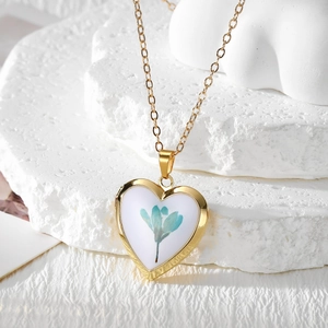 Bohemian gold heart locket necklace with blue dried flower on white textured stone