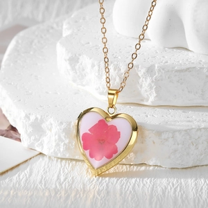 Macro detail of a heart-shaped gold locket necklace with an embedded red dried flower