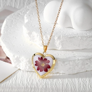 Detailed close-up of a heart-shaped golden resin pendant with real red dried flowers