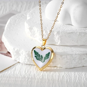 Close-up of golden heart resin pendant with green leaf dried flower on stone surface