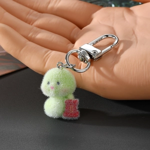 Detail of green plush snake keychain with soft faux fur texture and a lucky red charm