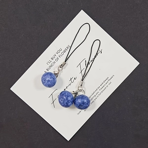 Detailed macro view of realistic resin blueberry charms with black straps on white card