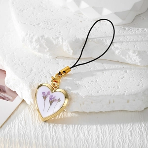Gros plan d'un pendentif cœur doré avec de vraies fleurs séchées violettes et cordon